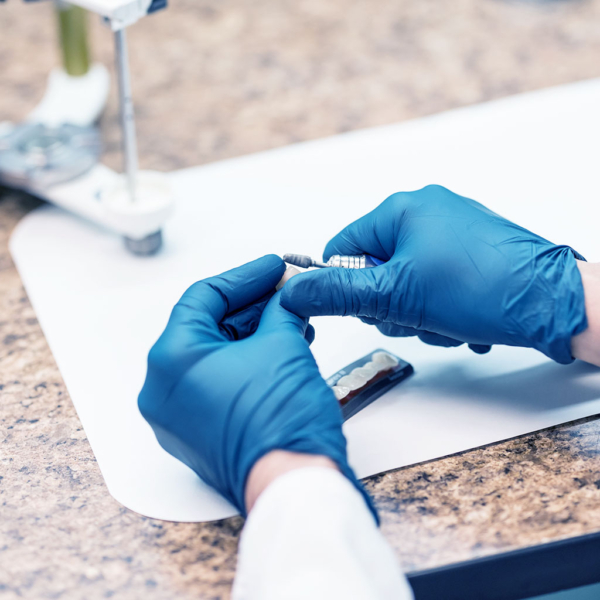 Hands wearing blue surgical gloves work with a small tool on tooth carving.